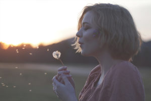 women blowing on dandelion